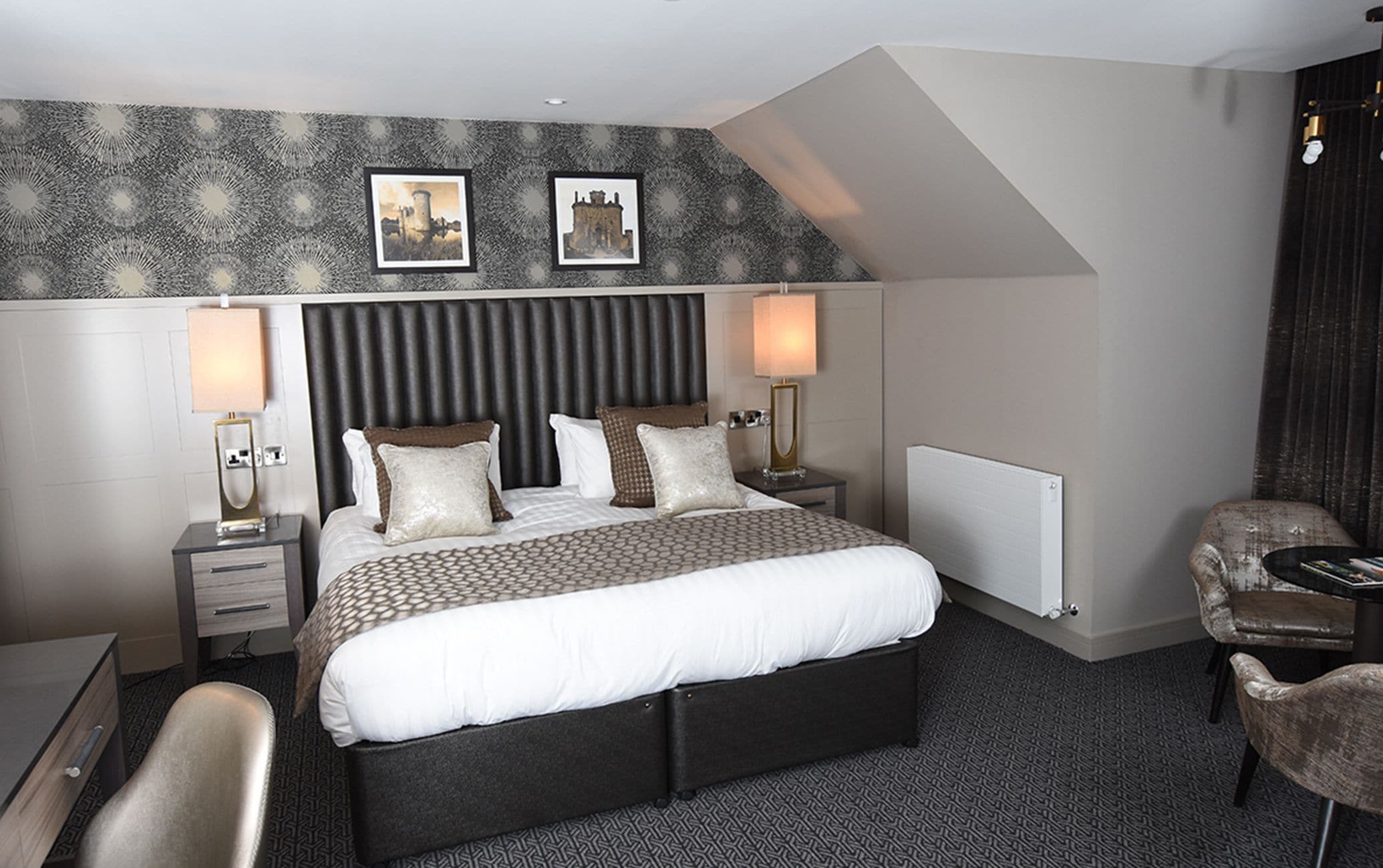 A modern hotel room with a large bed, two bedside tables with lamps, a chair, and a radiator.