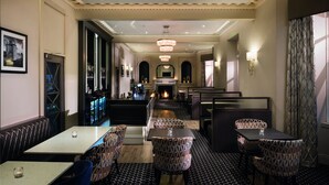 A restaurant with a long counter, patterned chairs, and a chandelier.