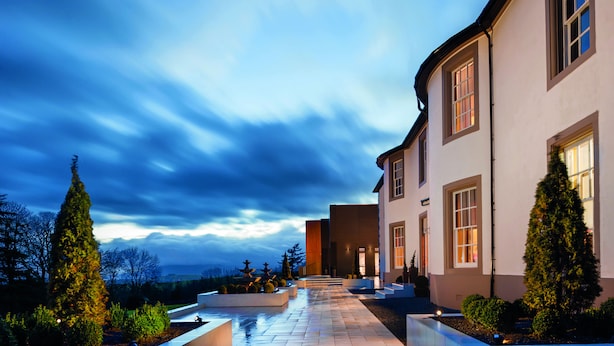 A modern house with a paved pathway leading to the entrance, surrounded by well-maintained greenery and a clear sky.