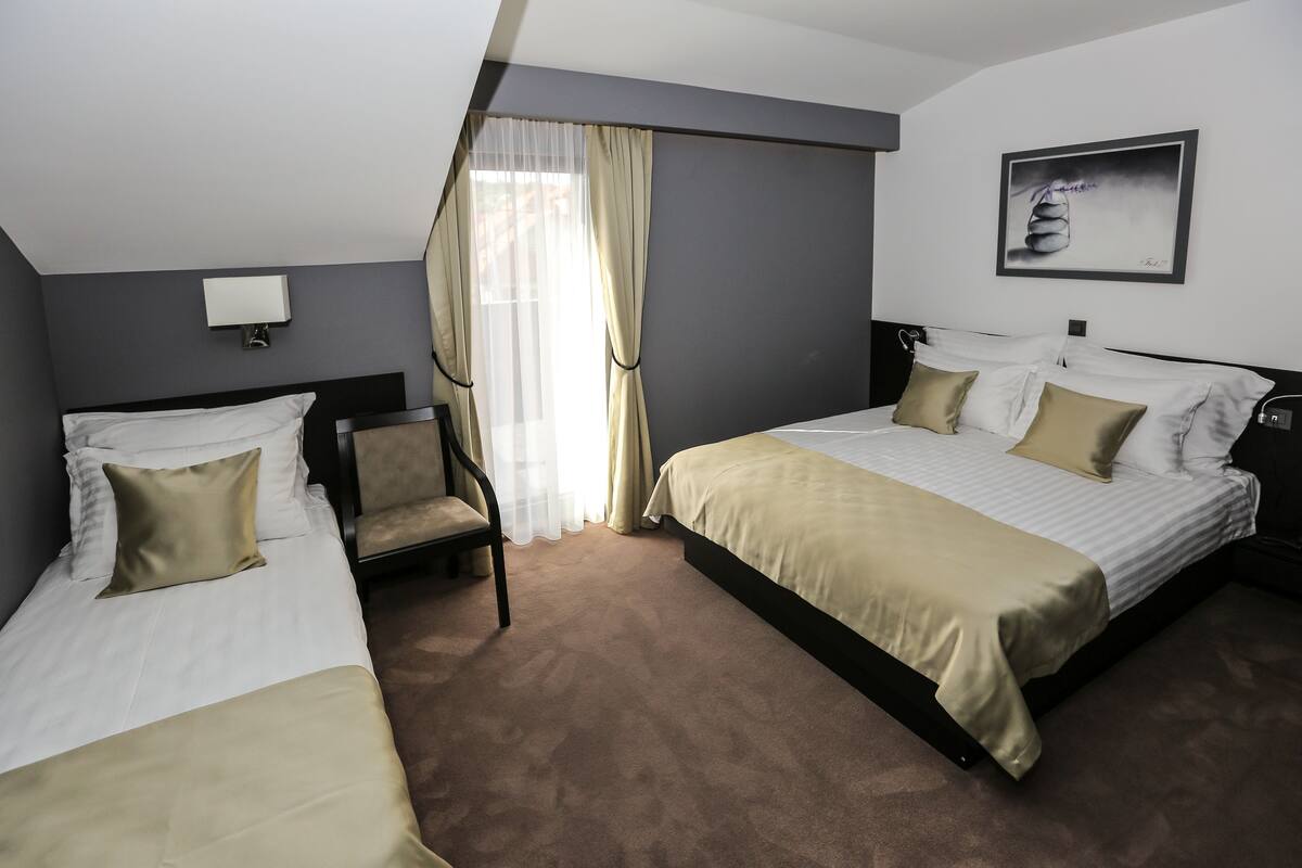 A hotel room with two beds, a chair, a desk, a lamp, and a painting on the wall.