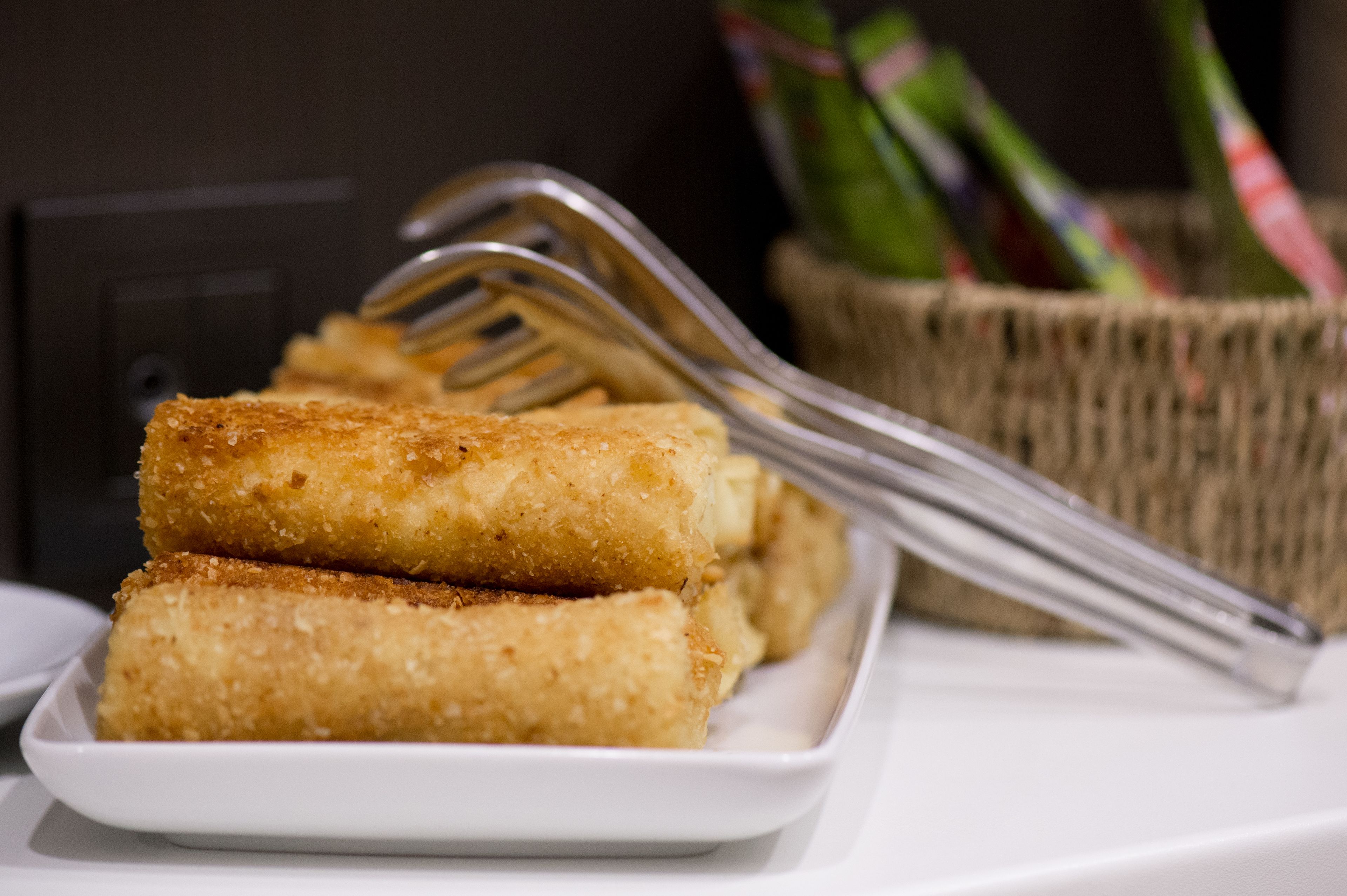 A plate of breaded and fried food items, likely croquettes, with a basket of green vegetables in the background.