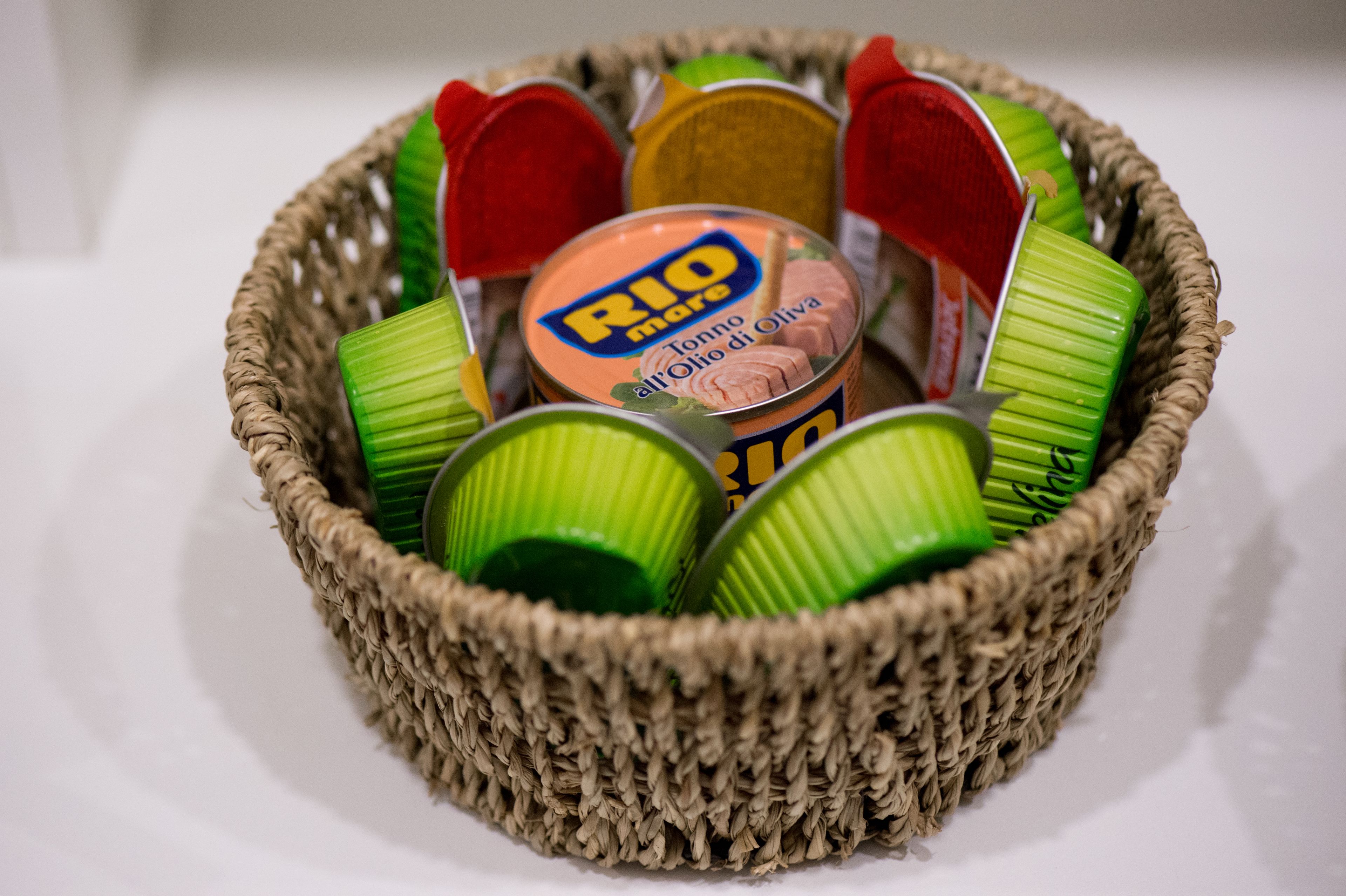 A woven basket containing various food items, including a tin labeled "RIO mare" and green cans.