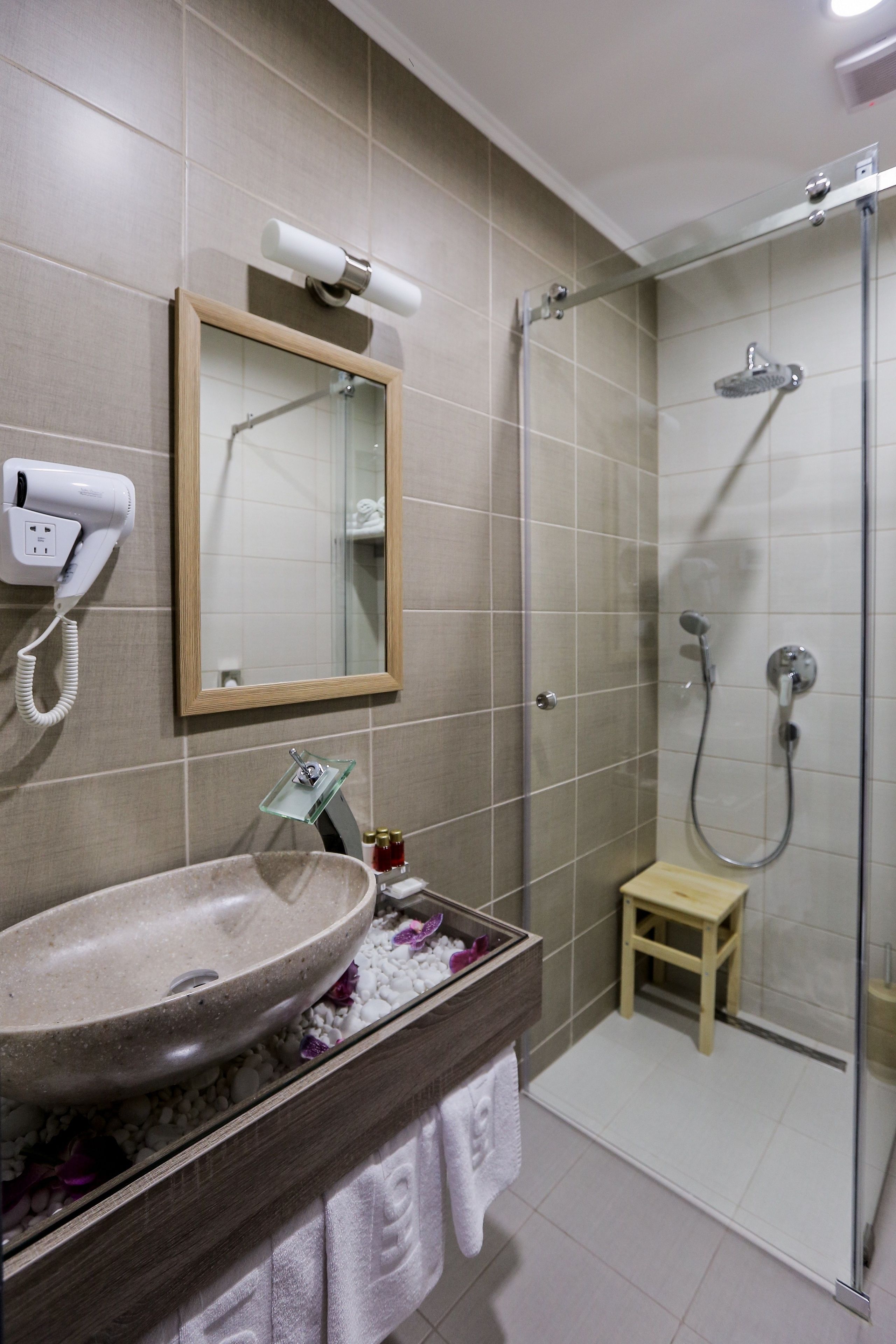 A bathroom with a sink, mirror, hairdryer, and shower.
