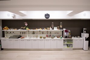 A modern kitchen with white cabinets, a coffee machine, and various food items displayed on shelves.