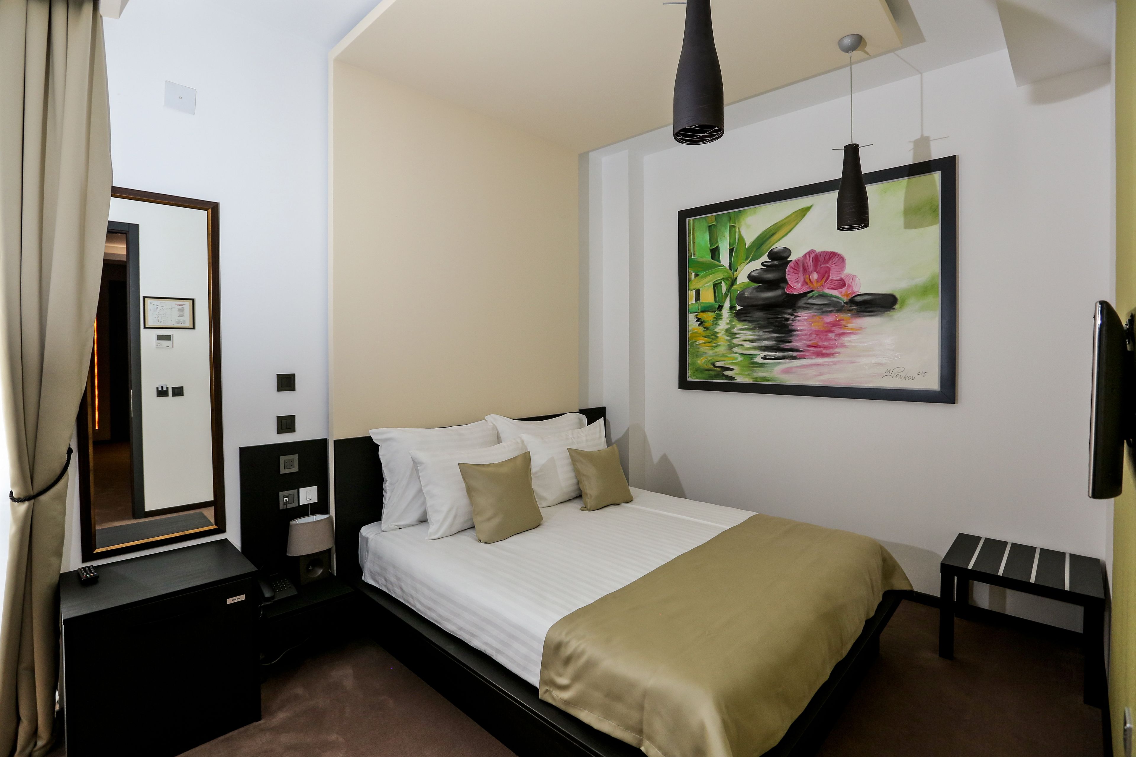 Ein Hotelzimmer mit Bett, Nachttisch, Lampe und einem Gemälde von einem Teich mit Blumen.