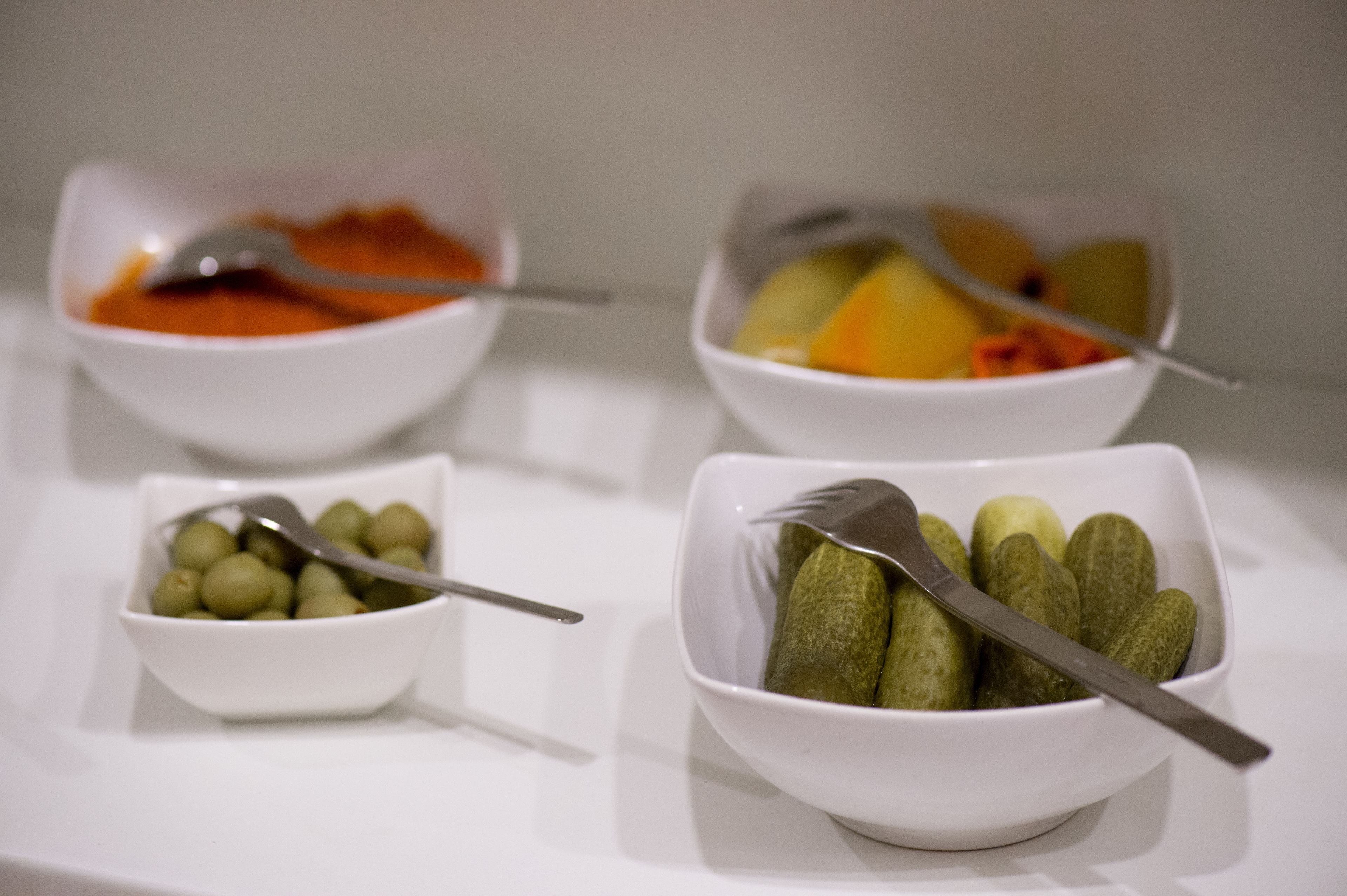 Three white bowls on a white surface, each containing different food items and a spoon.