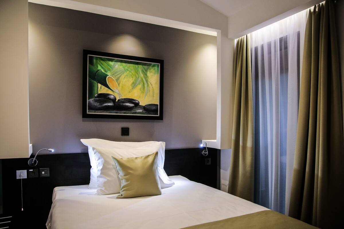 A hotel room with a bed, a painting on the wall, and curtains.