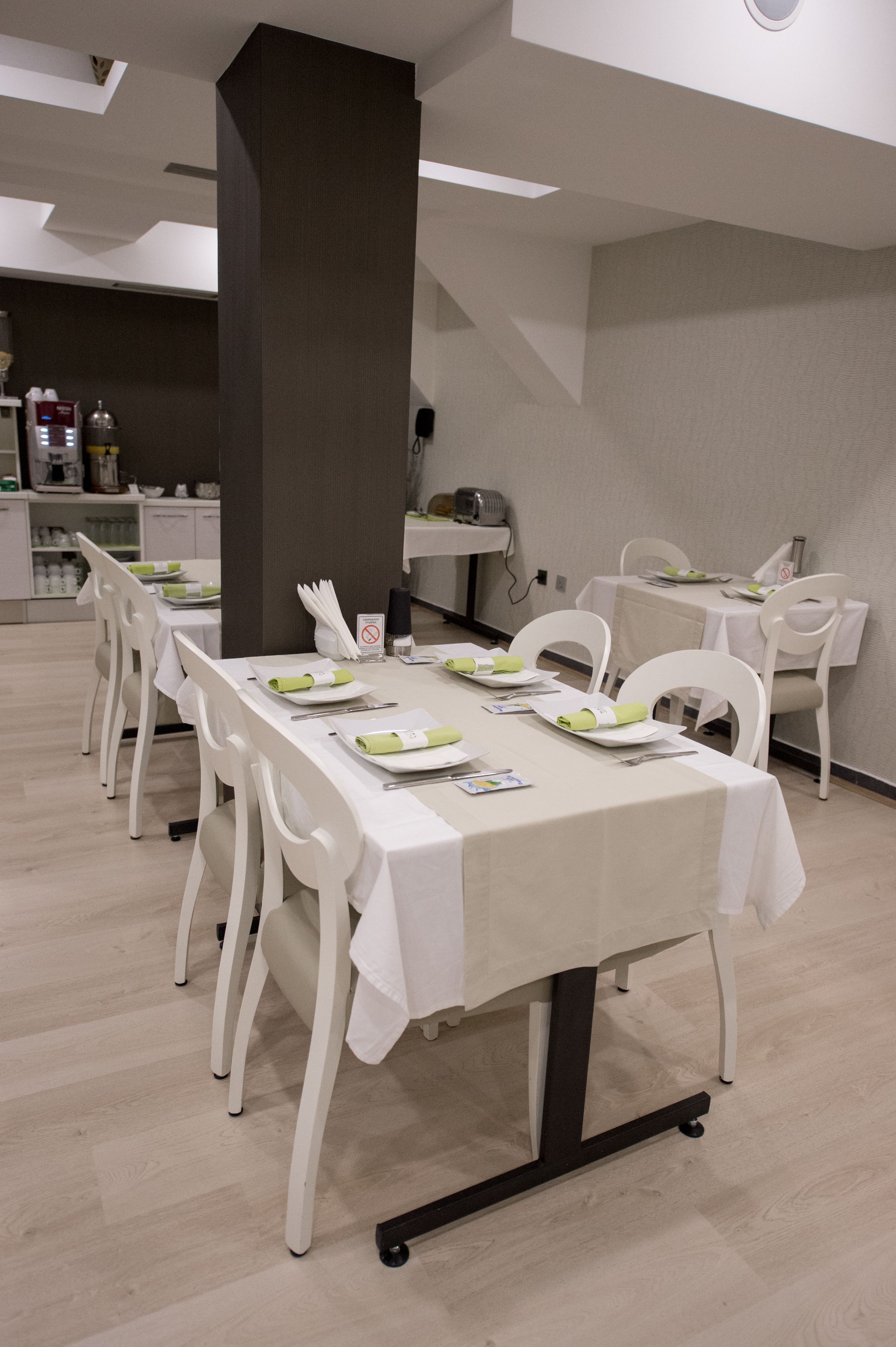 Un comedor con una mesa larga dispuesta para varias personas, sillas blancas y un pilar central.