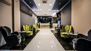 Un vestíbulo de hotel con un mostrador de recepción central, una zona de estar con sillas y mesas, y un suelo pulido.