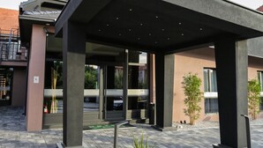 Un edificio moderno con entrada cubierta, ventanas amplias y un área pavimentada con plantas en macetas.