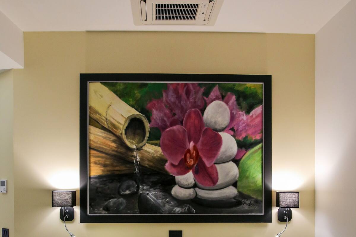 A hotel room with a bed, two wall-mounted lamps, a painting above the bed, and a ceiling vent.