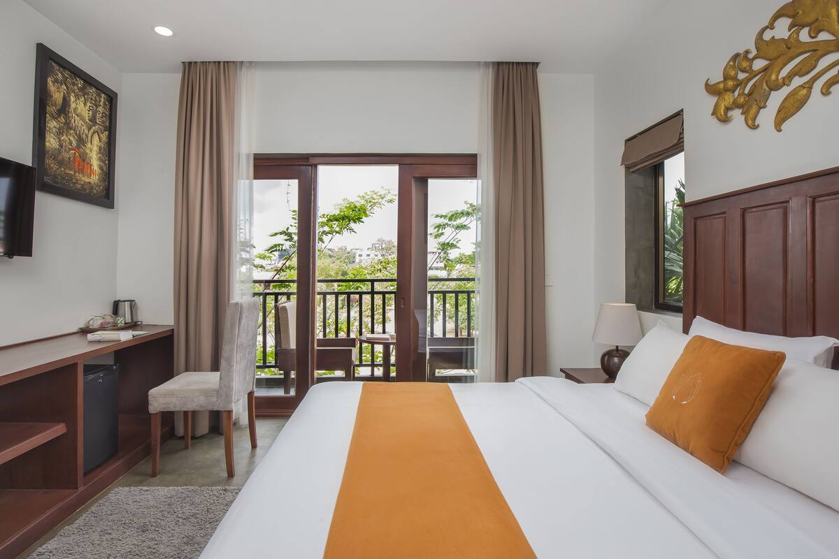 A hotel room with a bed, desk, chair, and a balcony with a view.