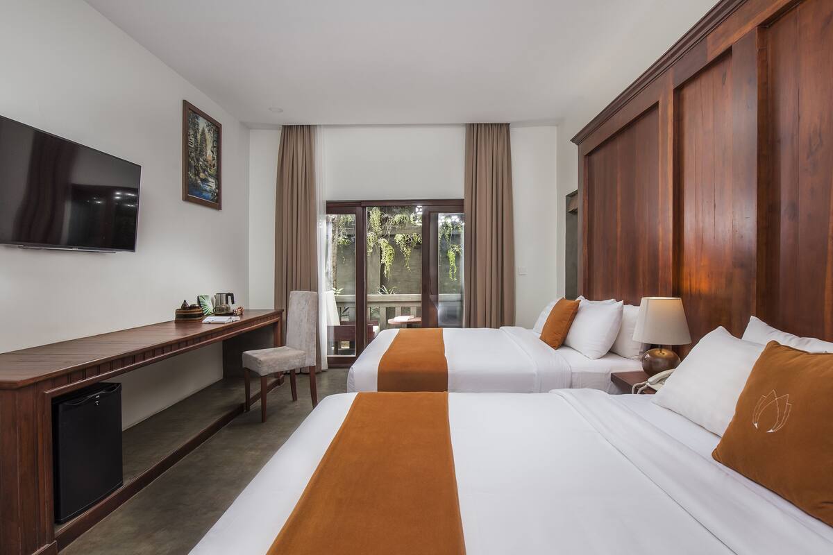 A hotel room with two beds, a desk, a television, and a view of the outdoors.