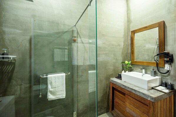 Un baño moderno con cabina de ducha de vidrio, tocador de madera con lavamanos y espejo sobre el tocador.