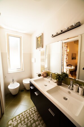 A bathroom with two sinks, a bidet, a window, a mirror, and a potted plant. - Villa Paganini B&B (Rome)