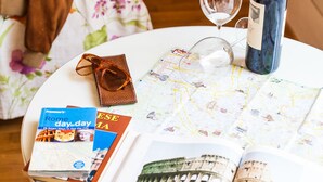 A round table with a wine bottle, a wine glass, a map, and travel books. - Villa Paganini B&B (Rome)