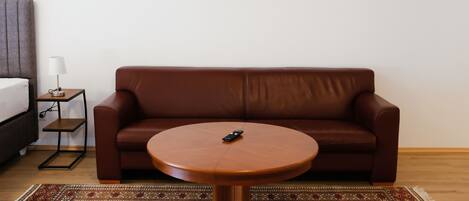 Une pièce moderne avec un canapé en cuir marron, une petite table ronde, une lampe et un tableau encadré au mur.