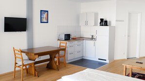 Une chambre moderne comprenant une table à manger en bois, deux chaises, un lit, un téléviseur, un coin cuisine avec des placards, un four à micro-ondes et une machine à café.