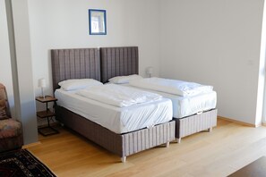 A double bed with a grey headboard, white bedding, and a small bedside table with a lamp. - MILCHHOF apartments (Aschaffenburg)