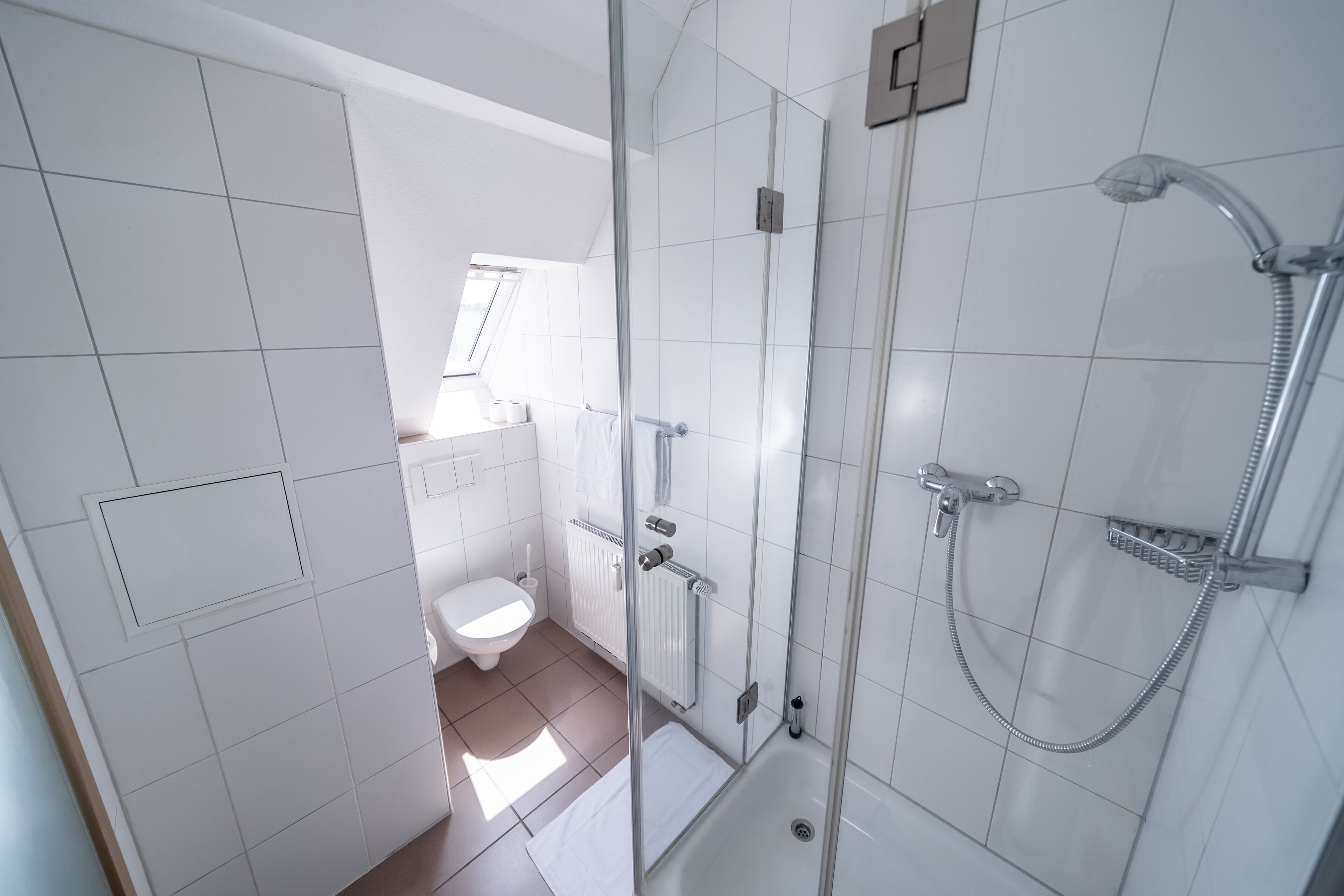 Een moderne badkamer met een douchecabine van glas, een toilet en een raam voor natuurlijk licht.