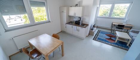 Cocina compacta con comedor, una mesa pequeña y una silla. Hay armarios, un microondas y un hervidor.