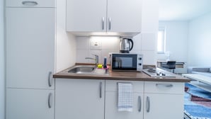 Une cuisine moderne avec des meubles blancs, un évier en acier inoxydable, un four à micro-ondes et une bouilloire.