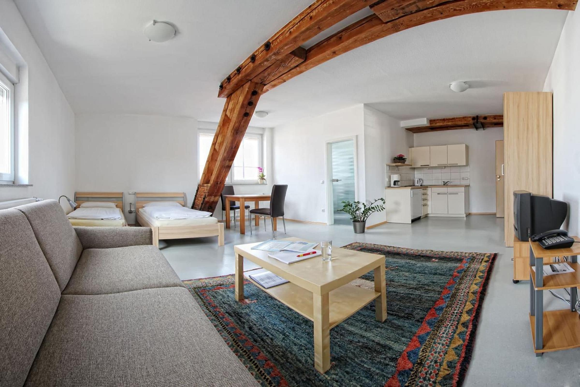 Eine moderne Wohnung mit Loft-Charakter, einem Wohnbereich mit Sofa und Couchtisch, einer Küche mit weißen Schränken sowie einem Essbereich mit Tisch und Stühlen.