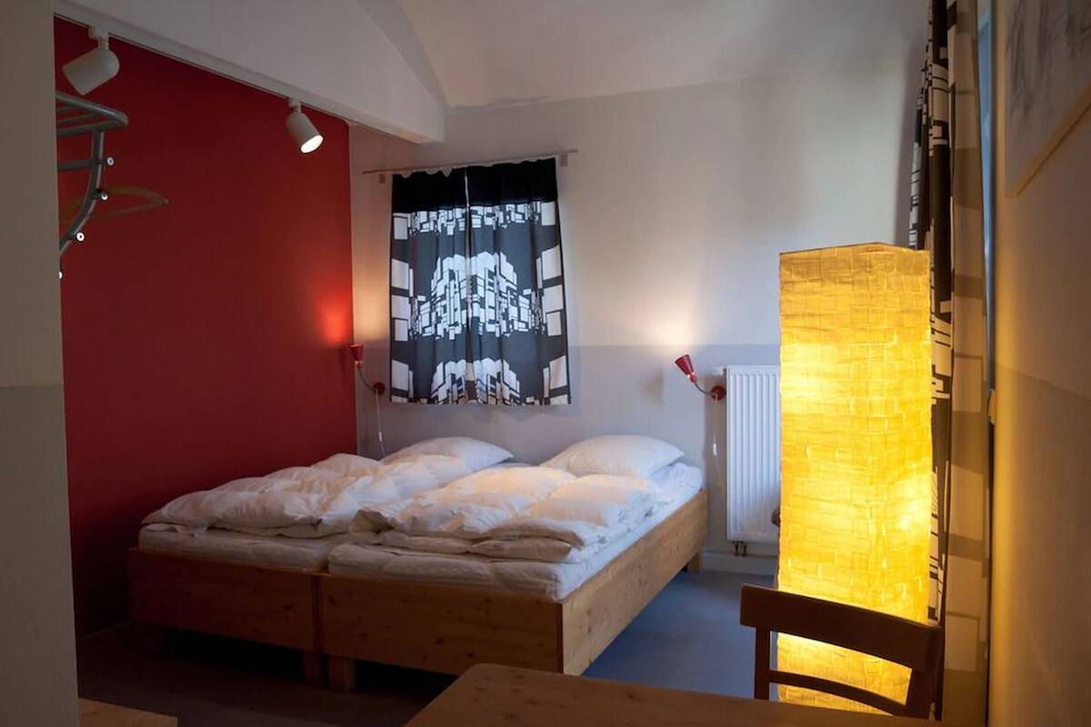 Une chambre à coucher avec un lit, un mur rouge, une tapisserie en noir et blanc et une table avec une chaise.