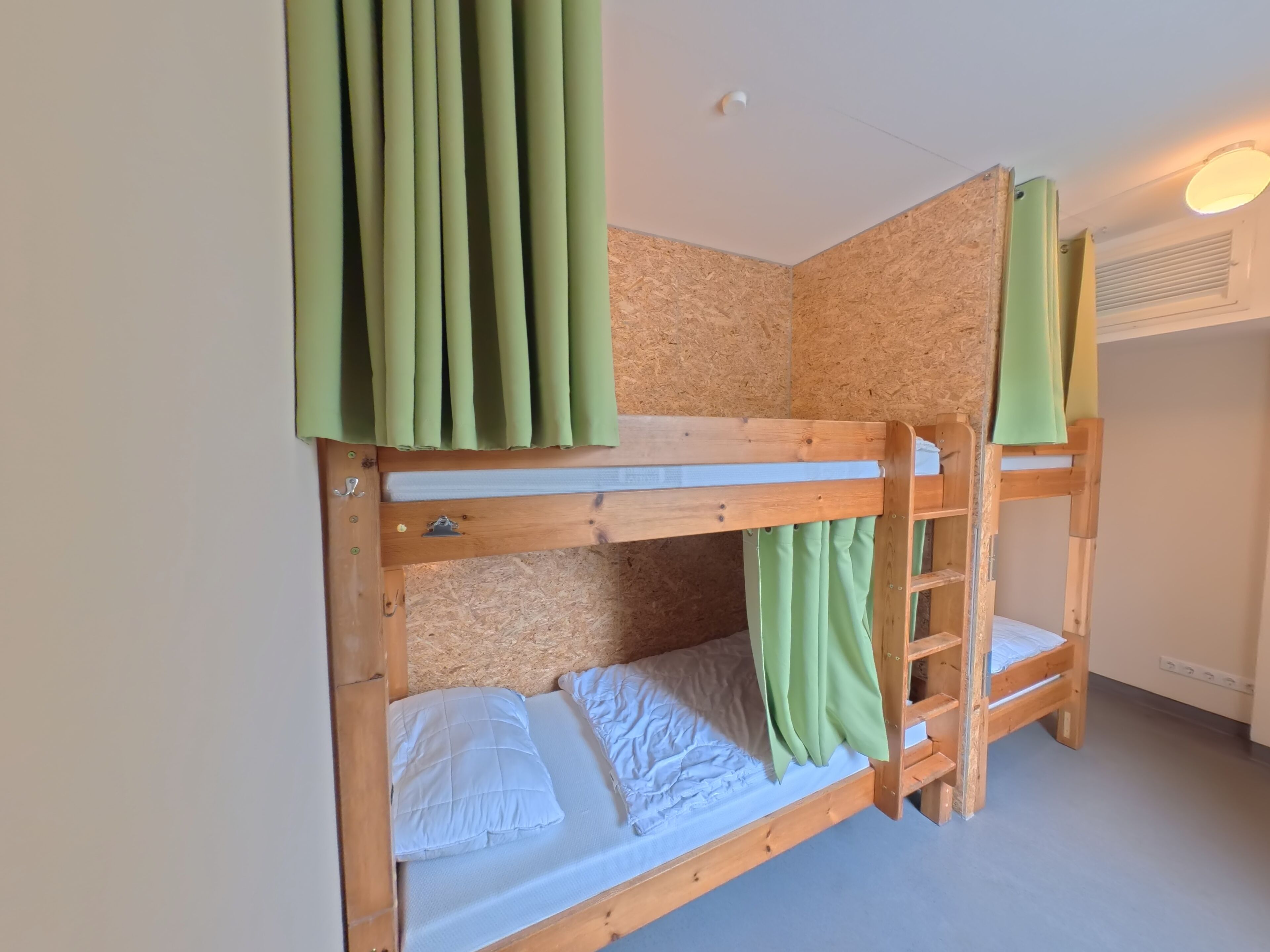 A bunk bed with a wooden frame, a lower bunk with a mattress and pillows, and a top bunk with a curtain.