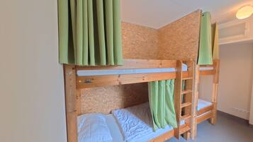 A bunk bed with a wooden frame, a lower bunk with a mattress and pillows, and a top bunk with a curtain.