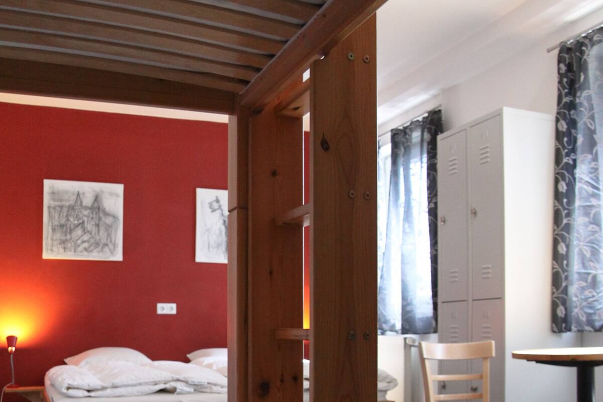 Une pièce comprenant un lit, un bureau et une chaise. On y trouve également des casiers et une fenêtre avec des rideaux.