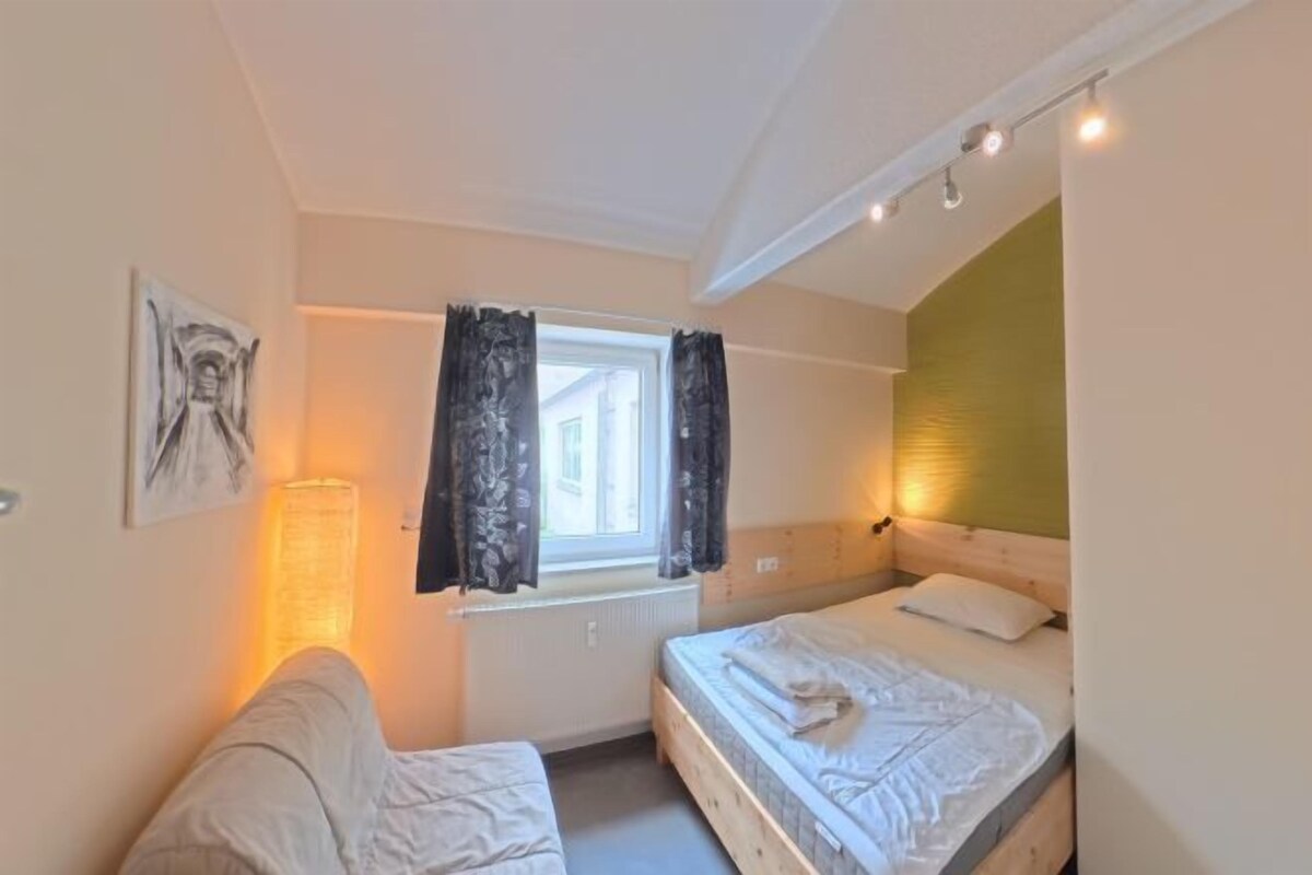 A bedroom with two beds, a window with curtains, a bedside lamp, and a wall-mounted artwork.