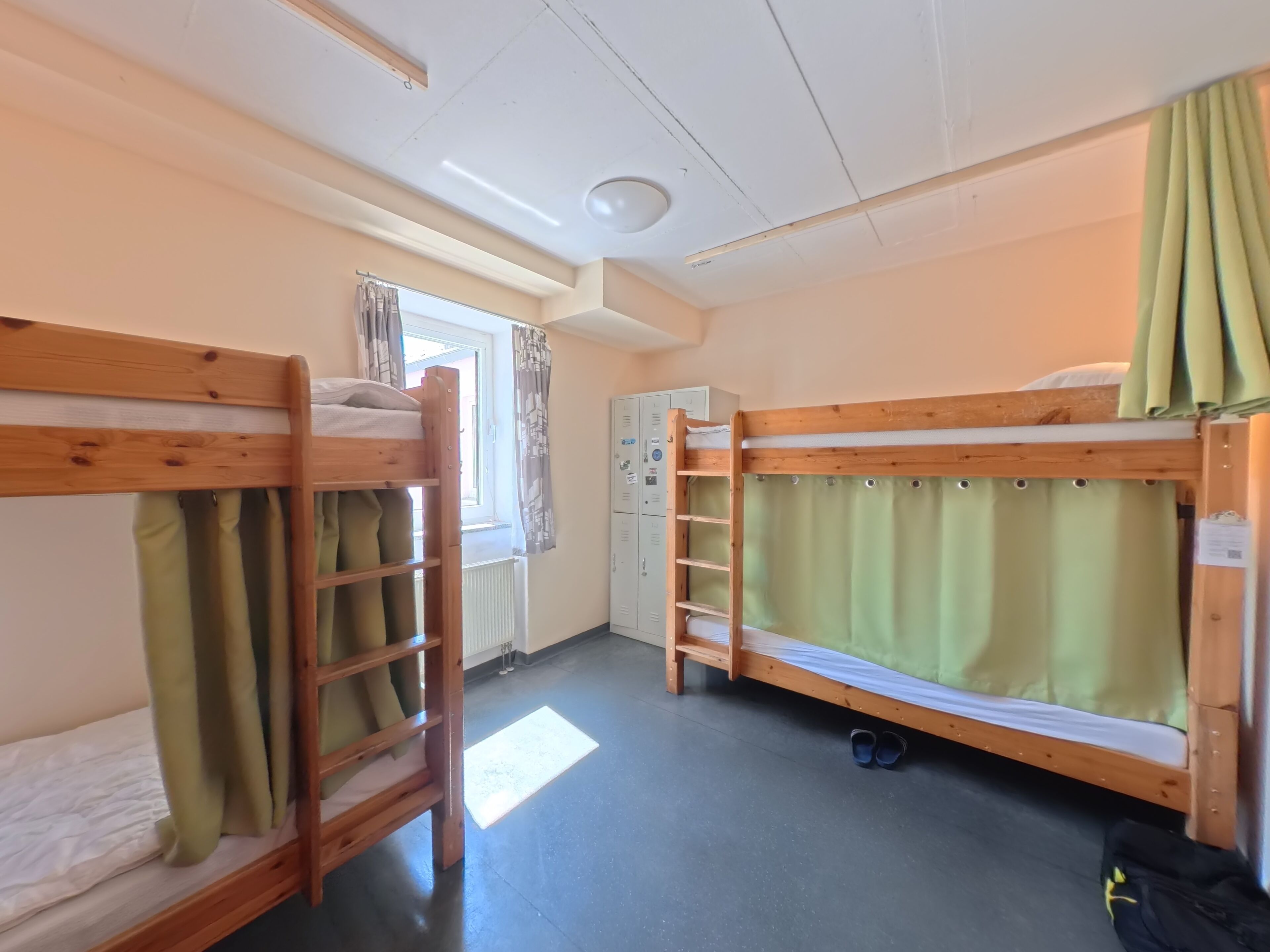 Ein Schlafraum mit Etagenbetten, einem Heizkörper, einem Fenster mit Vorhängen und einem Kleiderschrank.