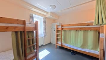 Ein Schlafraum mit Etagenbetten, einem Heizkörper, einem Fenster mit Vorhängen und einem Kleiderschrank.