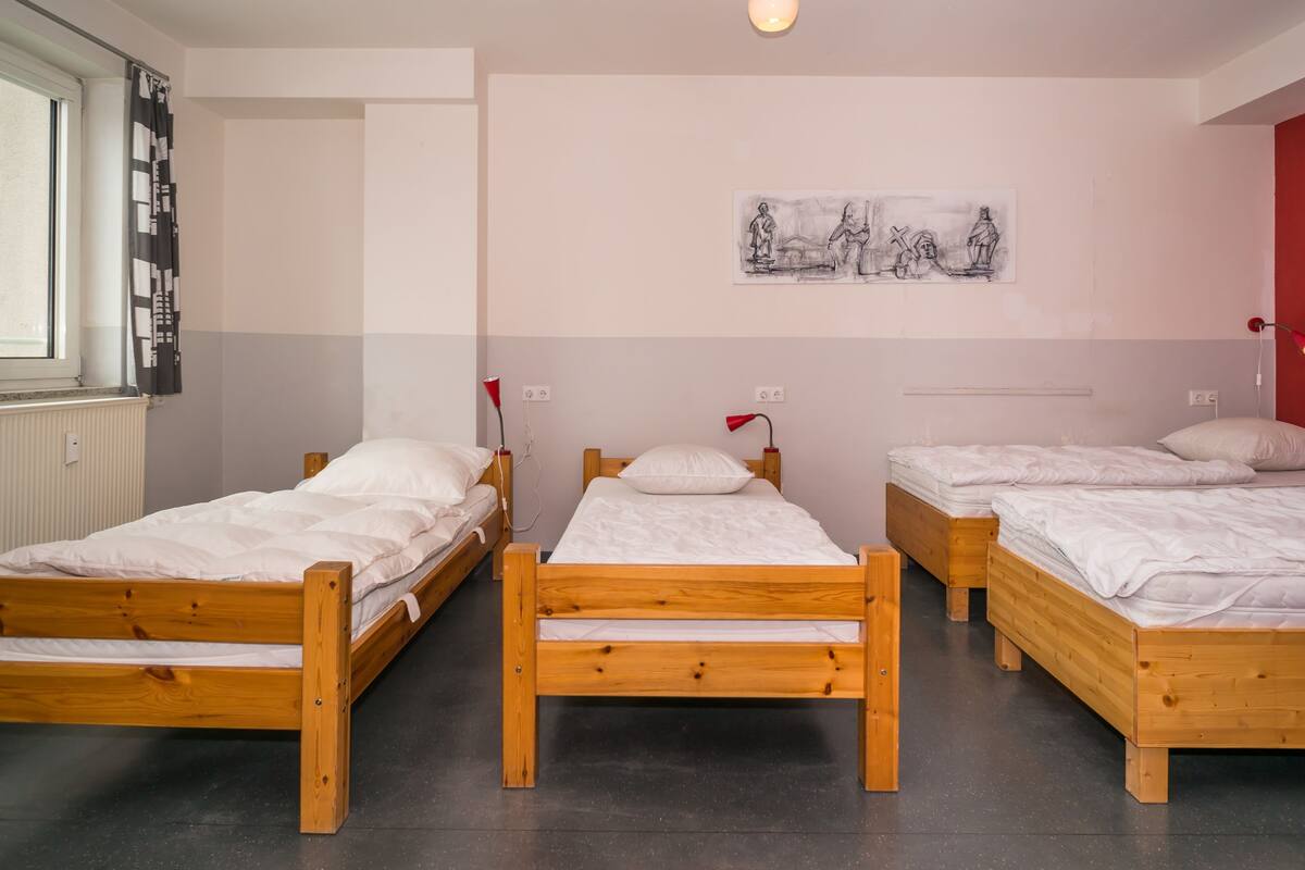 Une chambre de dortoir avec trois lits en bois, un mur rouge et une fenêtre avec des rideaux.