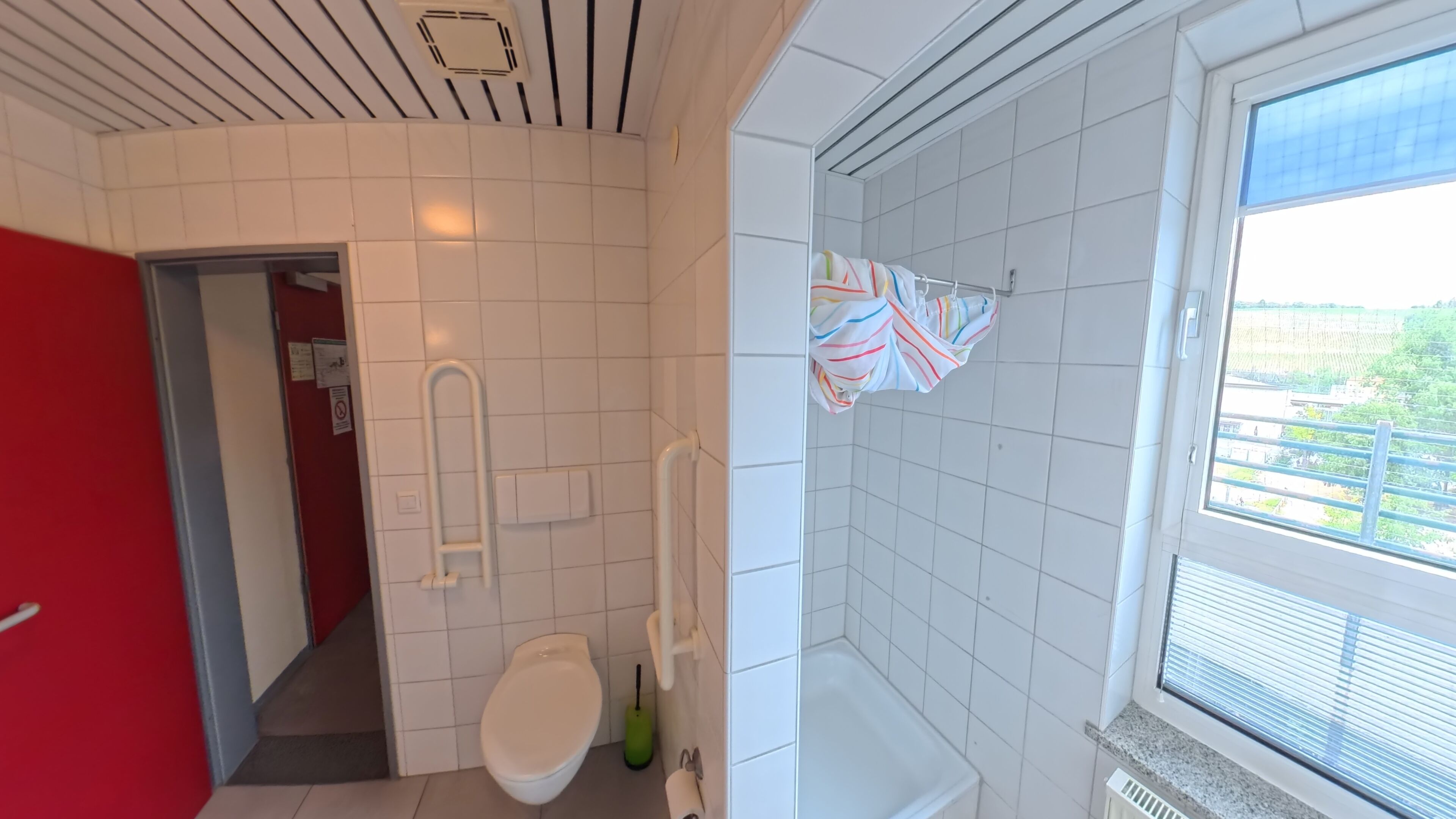 Un baño con inodoro, ducha, ventana y toallero.