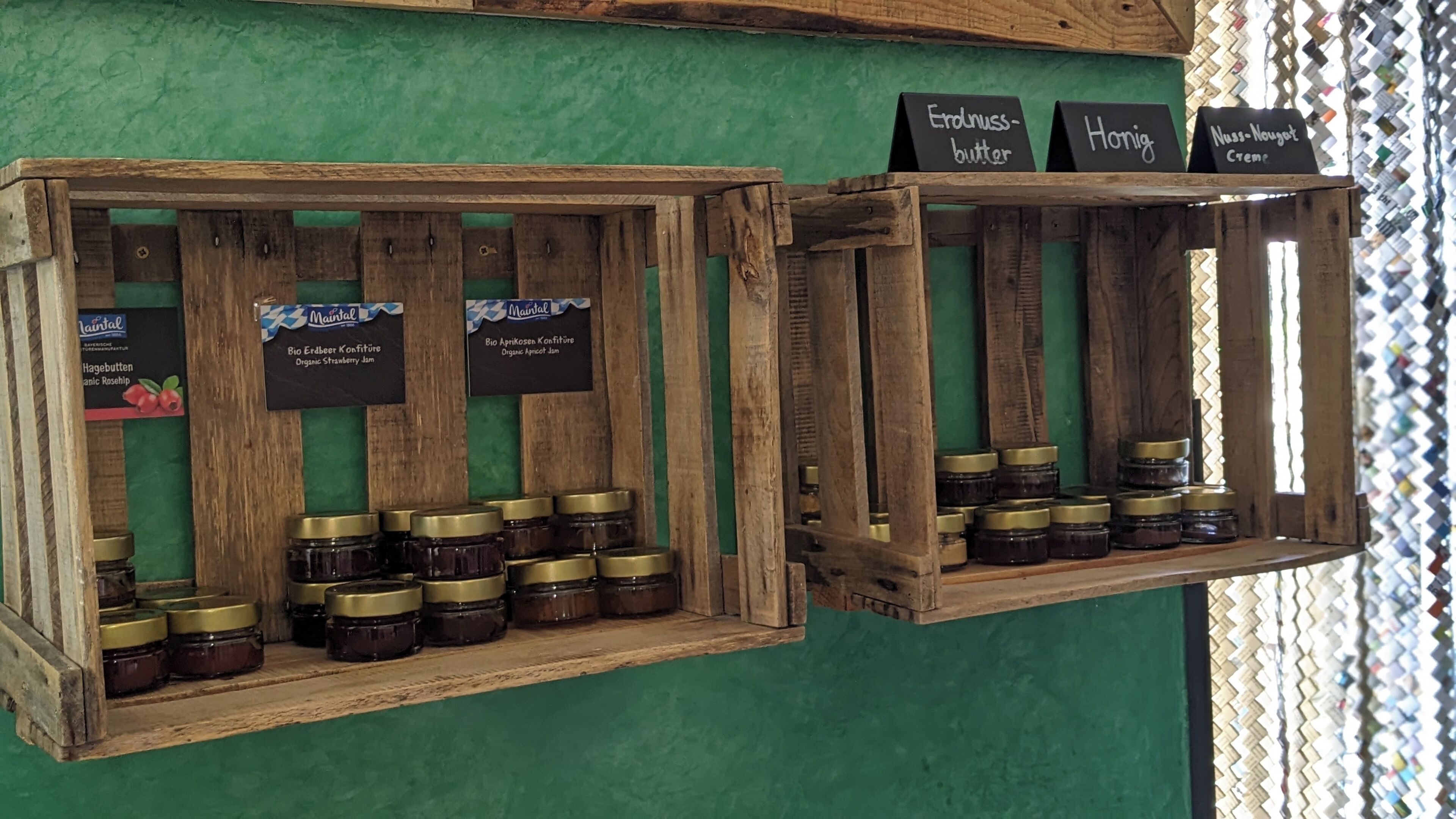 Two wooden display shelves with jars of preserves and labels indicating names like 'Erdnussbutter' and 'Honig'.