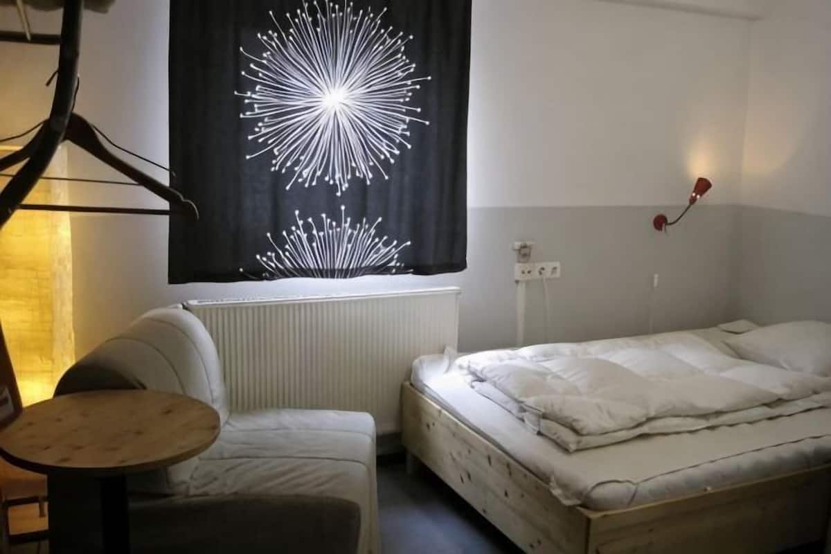 Une petite piÚce simple, avec un lit, une chaise, une table et un luminaire fixé au mur.