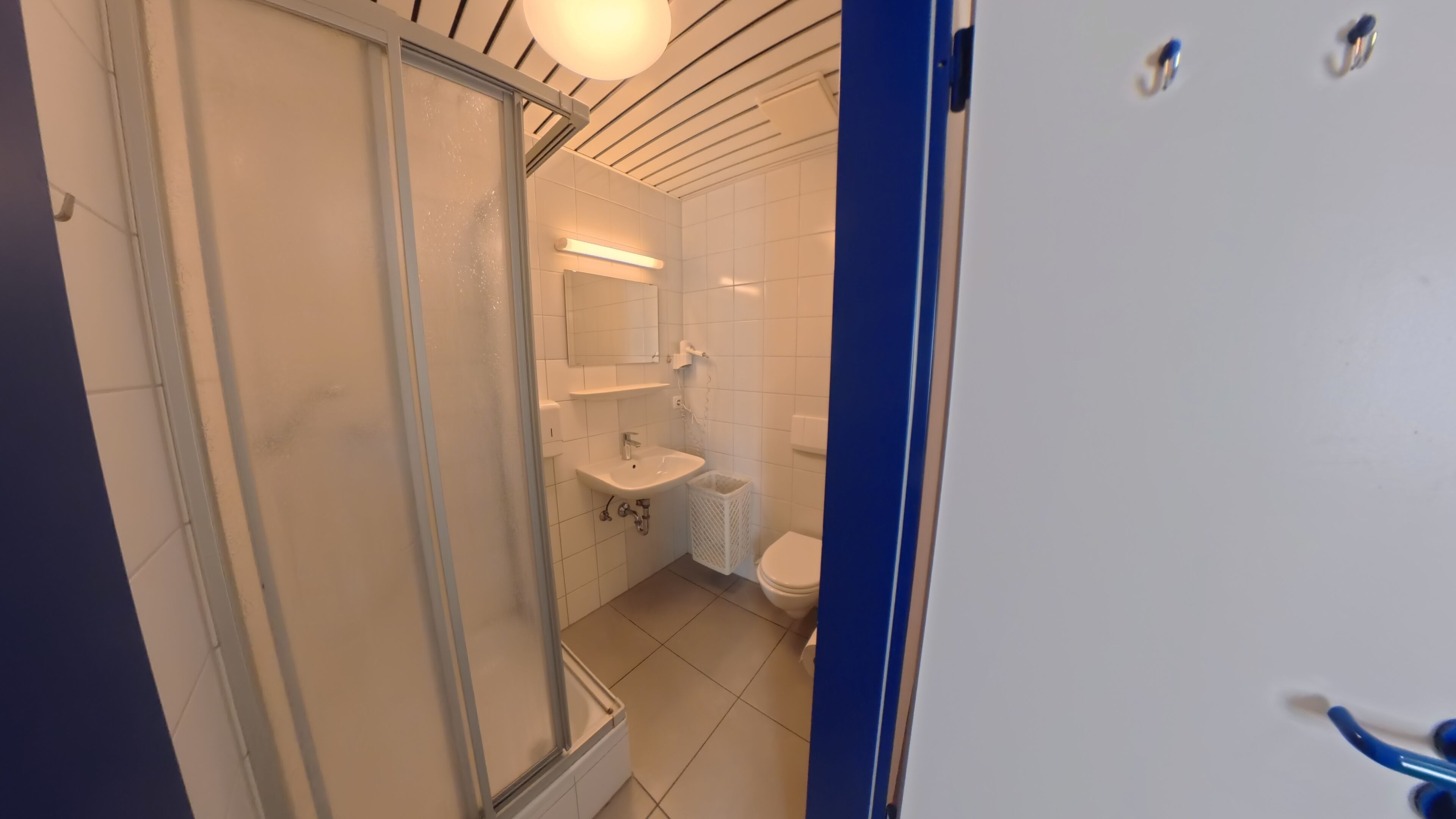 Um banheiro com box de vidro, pia, vaso sanitário e espelho.