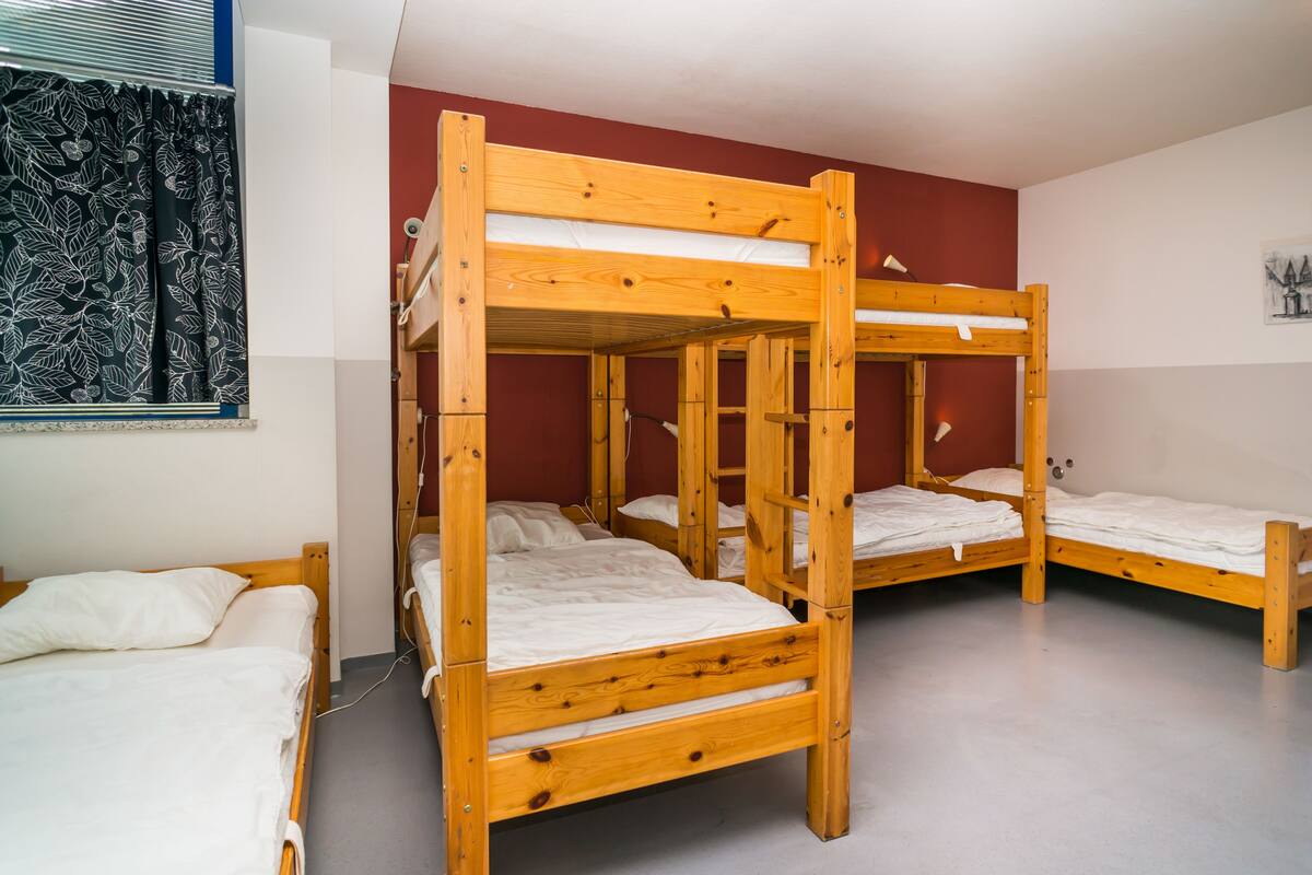 Une chambre de dortoir avec des lits superposés, une fenêtre ornée de rideaux à motifs et une lampe fixée au mur.