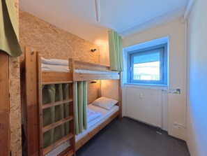 Dormitorio con literas, ventana, radiador y pared de madera.