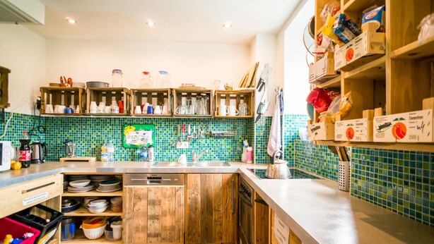 A kitchen with wooden cabinets, a tiled backsplash, and various kitchen utensils and appliances. - Babelfish Hostel (Würzburg)
