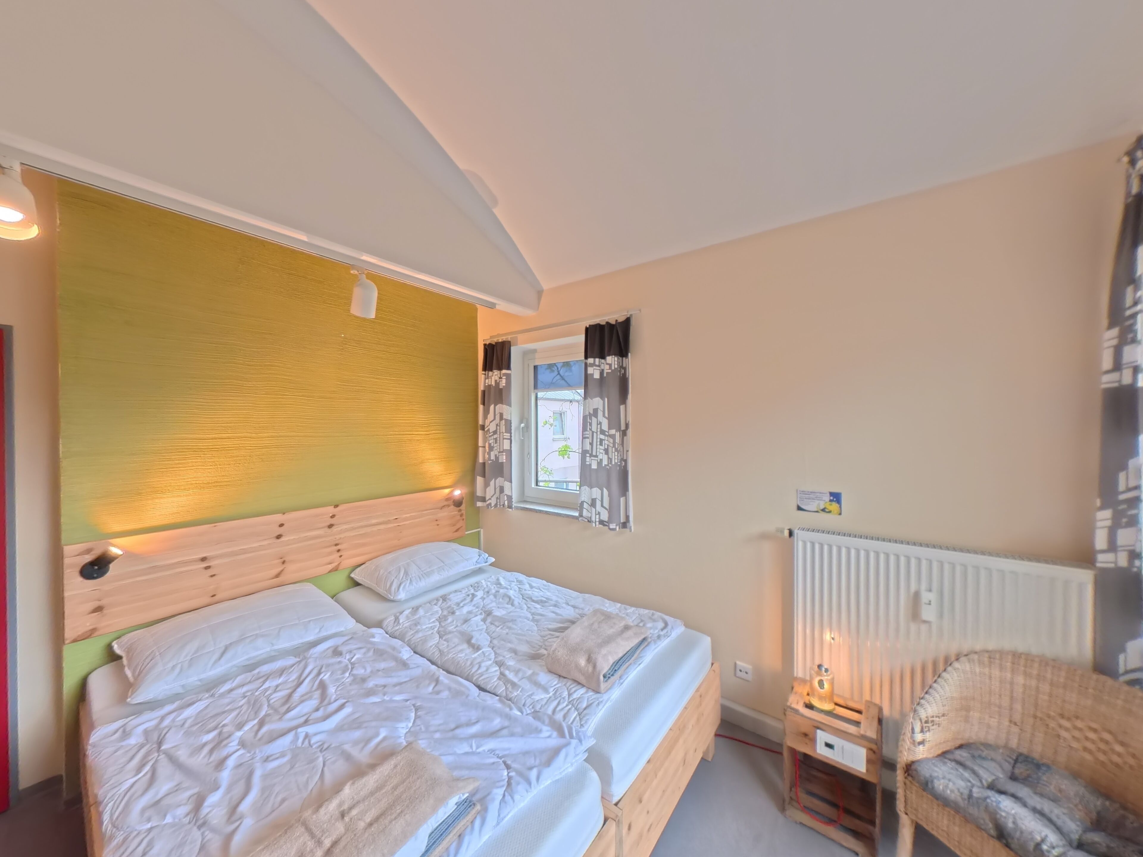 A double bed with a wooden headboard, a bedside table with a lamp, and a wicker chair.