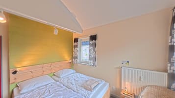 A double bed with a wooden headboard, a bedside table with a lamp, and a wicker chair.