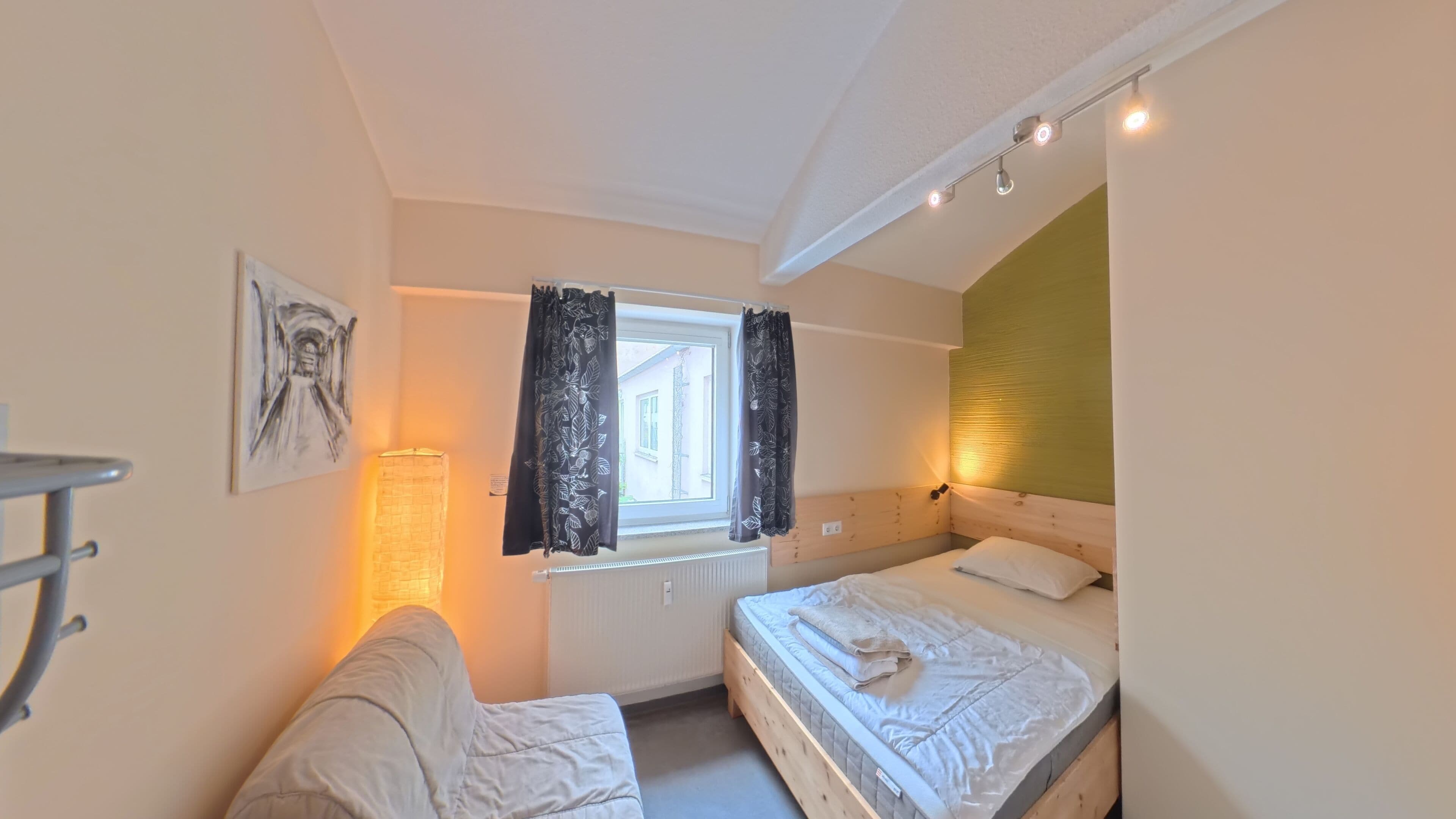 A bedroom with two beds, a window with curtains, a radiator, and a wall-mounted light fixture.