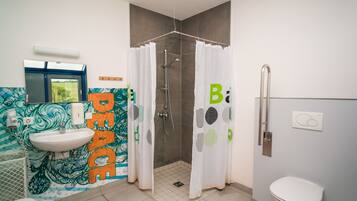 Ein Badezimmer mit Waschbecken, Toilette, Dusche und einer Wand mit einem farbenfrohen Wandgemälde.