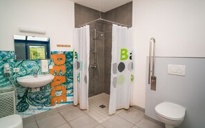 Un baño con lavamanos, inodoro, ducha y una pared con un mural colorido.
