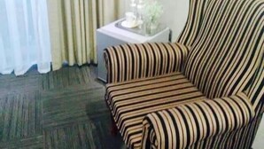 A striped armchair, a small table with a cup and a vase, and a TV mounted on the wall. - Shawu Lodge & Conference (Bloemfontein)