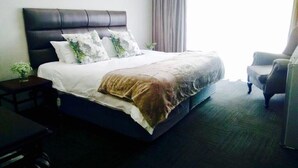 A hotel room with a large bed, a chair, and a small table. - Shawu Lodge & Conference (Bloemfontein)
