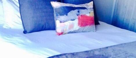A bed with a dark headboard, a blue pillow, and a colorful throw pillow.